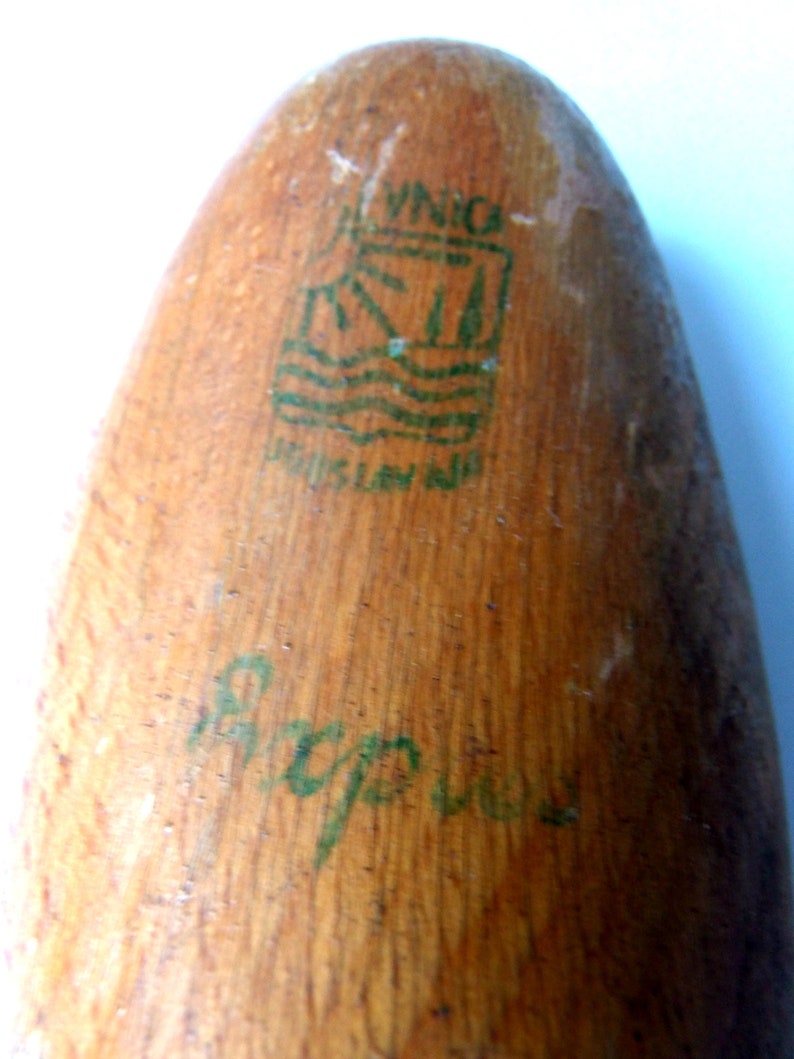 K&ouml;nnte beinhalten: Nahaufnahme eines Holzobjekts mit abgerundetem Ende. Die Holzmaserung ist sichtbar. Ein gr&uuml;nes Logo und Text sind auf die Oberfl&auml;che gedruckt, mit zus&auml;tzlichem gr&uuml;nen Schriftzug darunter. Das Logo scheint eine stilisierte Landschaft darzustellen.