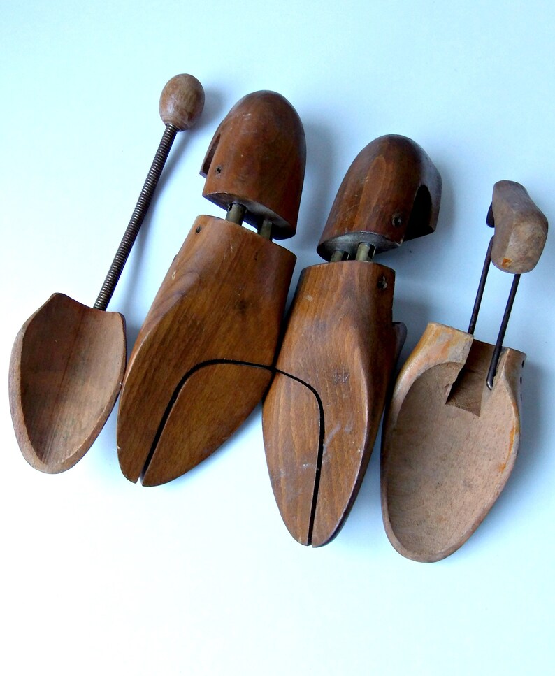 K&ouml;nnte beinhalten: Vier Schuhspanner aus Holz in verschiedenen Designs. Sie bestehen aus dunkelbraunem Holz und verf&uuml;gen &uuml;ber Metall- und Federmechanismen. Ein Spanner hat einen langen Griff mit einem Holzkopf. Auf wei&szlig;em Hintergrund.