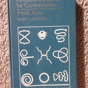 May include: A teal book titled "Intrauterine Devices for Contraception" with gold lettering. The cover features white line drawings of various shapes and the text "THE IUD".