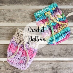 May include: Two crocheted bags, one in shades of pink and purple, the other in a rainbow of colors. The bags are on a wooden surface with the text "Crochet Pattern" in a white circle.