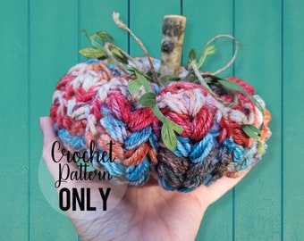 May include: A crocheted pumpkin with a rustic wooden stem, featuring a mix of red, blue, white, and brown yarn. The pumpkin is held in a hand against a teal background. The text "Crochet Pattern ONLY" is visible in the image.