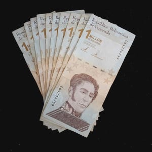 May include: A fan of Venezuelan 1 million Bolivar banknotes. Each bill features a portrait of a man and the text "República Bolivariana de Venezuela". The bills are beige with a portrait and star pattern.