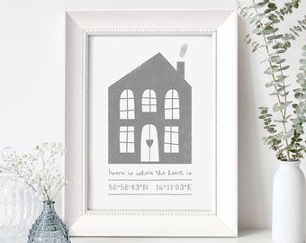 May include: A white framed print with a gray illustration of a house with a heart in the window. The text "home is where the heart is" and the coordinates "50°58′43″N 16°11'03 E" are printed below the house.