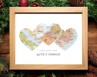 Może przedstawiać: Wydruk w ramie z trzema mapami w kształcie serca z różnych miejsc. Mapy są w odcieniach niebieskiego, zielonego i brązowego. Tekst "Kate & Thomas" i trzy daty są wydrukowane pod mapami.