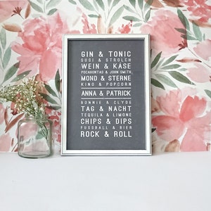 Puede incluir: Una impresi&oacute;n enmarcada en blanco con fondo gris y texto blanco. El texto dice "Gin & Tonic, Susi & Strolch, Wein & K&auml;se, Pocahontas & John Smith, Mond & Sterne, Kino & Popcorn, Anna & Patrick, Bonnie & Clyde, Tag & Nacht, Tequila & Limone, Chips & Dips, Fussball & Bier, Rock & Roll".