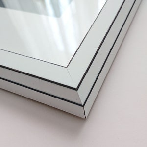 Puede incluir: Primer plano de la esquina de un marco de imagen blanco con un doble borde negro. El marco est&aacute; hecho de madera y tiene un acabado liso y brillante.