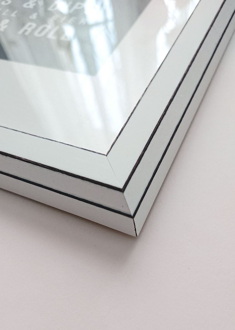 Puede incluir: Primer plano de la esquina de un marco de imagen blanco con un doble borde negro. El marco est&aacute; hecho de madera y tiene un acabado liso y brillante.
