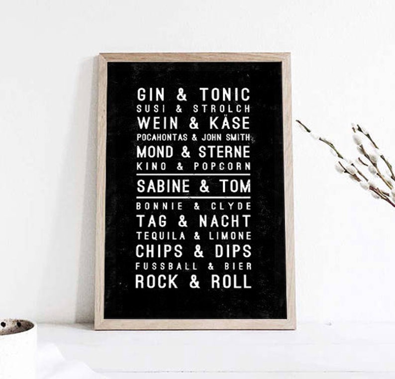 May include: A framed black and white print with a list of phrases in white text. The phrases include "GIN & TONIC", "WEIN & KASE", "MOND & STERNE", "SABINE & TOM", "BONNIE & CLYDE", "TAG & NACHT", "TEQUILA & LIMONE", "CHIPS & DIPS", "FUSSBALL & BIER", and "ROCK & ROLL".