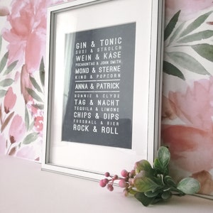 Puede incluir: Una impresi&oacute;n enmarcada en blanco con fondo negro y texto blanco. El texto dice "Gin & Tonic, Susi & Strolch, Wein & Kase, Pocahontas & John Smith, Mond & Sterne, Kino & Popcorn, Anna & Patrick, Bonnie & Clyde, Tag & Nacht, Tequila & Limone, Chips & Dips, Fussball & Bier, Rock & Roll".