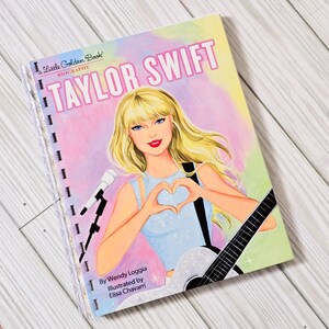 May include: A Little Golden Book biography of Taylor Swift featuring a blonde illustration of the singer making a heart shape with hands, holding a guitar, and standing by a microphone. The cover has pink, yellow, and green watercolor accents.