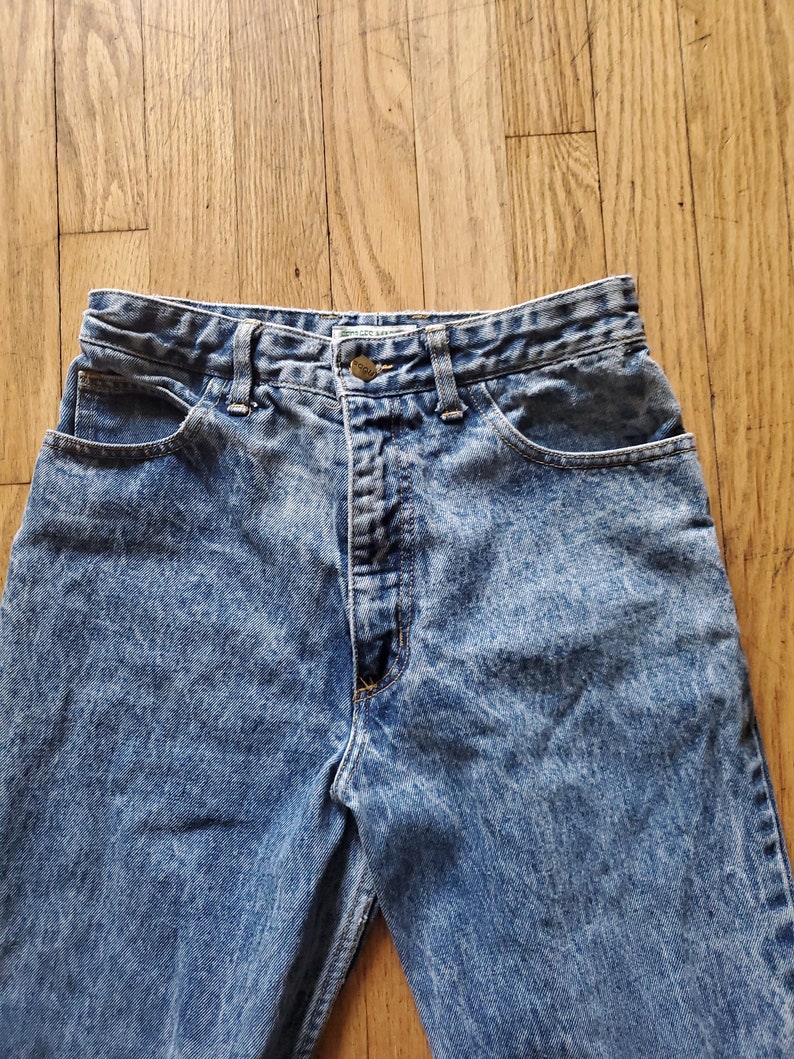 May include: A pair of light blue acid wash denim jeans with a button fly and five pockets.