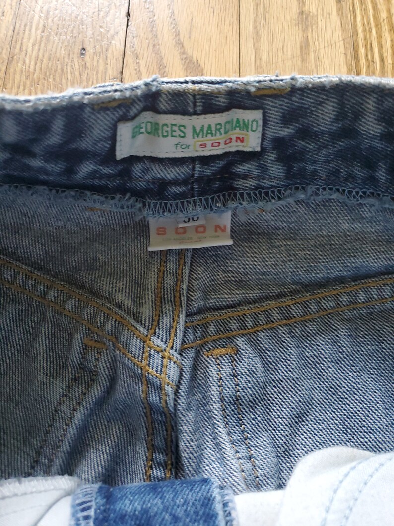 May include: Light blue denim jeans with a green label that reads "Georges Marciano for SOON" and a white label that reads "SOON 30".