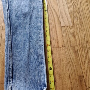 May include: A pair of light blue acid wash jeans with a yellow measuring tape next to them. The tape measures 39 inches.