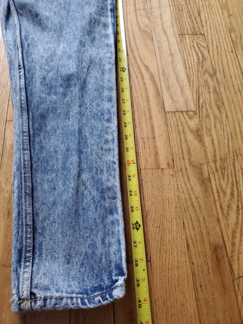 May include: A pair of light blue acid wash jeans with a yellow measuring tape next to them. The tape measures 39 inches.