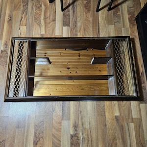 May include: A rectangular, dark brown wall-mounted cabinet with a mirrored back and two shelves. The cabinet has a decorative metal mesh on each side and is set against a wooden plank background.