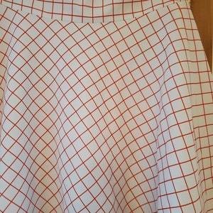 May include: A white skirt with a red grid pattern and a red trim around the bottom.