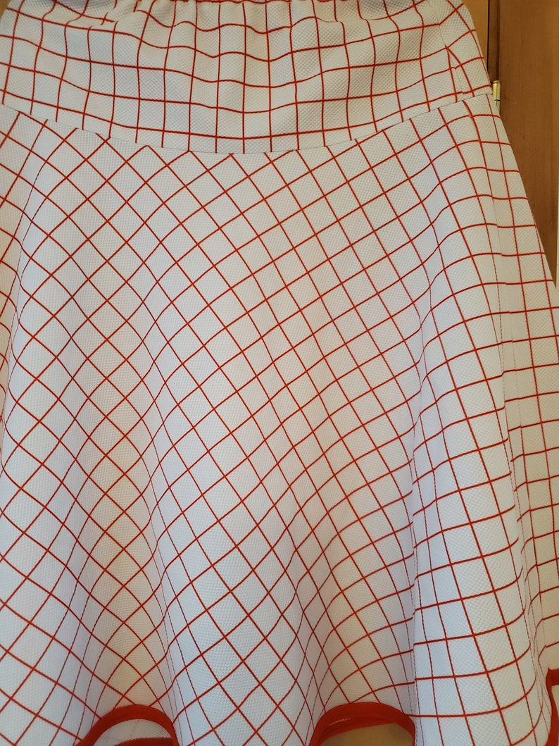 May include: A white skirt with a red grid pattern and a red trim around the bottom.