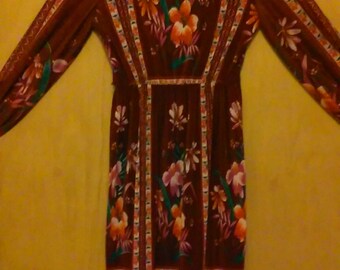 Peut inclure: Une robe longue à manches longues de couleur marron avec un imprimé floral. La robe a une taille cintrée et une jupe ample. Les fleurs sont dans des tons de rose, orange et vert.