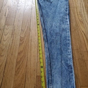 May include: Light blue acid wash denim jeans with a yellow measuring tape next to them. The tape measures 30 inches.