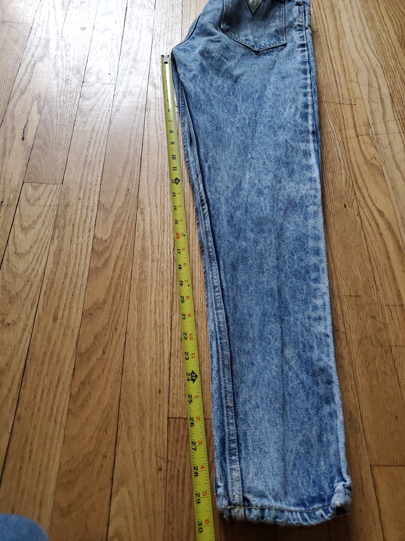 May include: Light blue acid wash denim jeans with a yellow measuring tape next to them. The tape measures 30 inches.