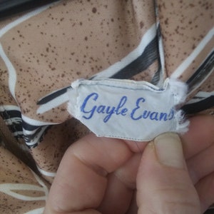 May include: A white tag with blue text that reads "Gayle Evans" on a brown and white striped fabric.