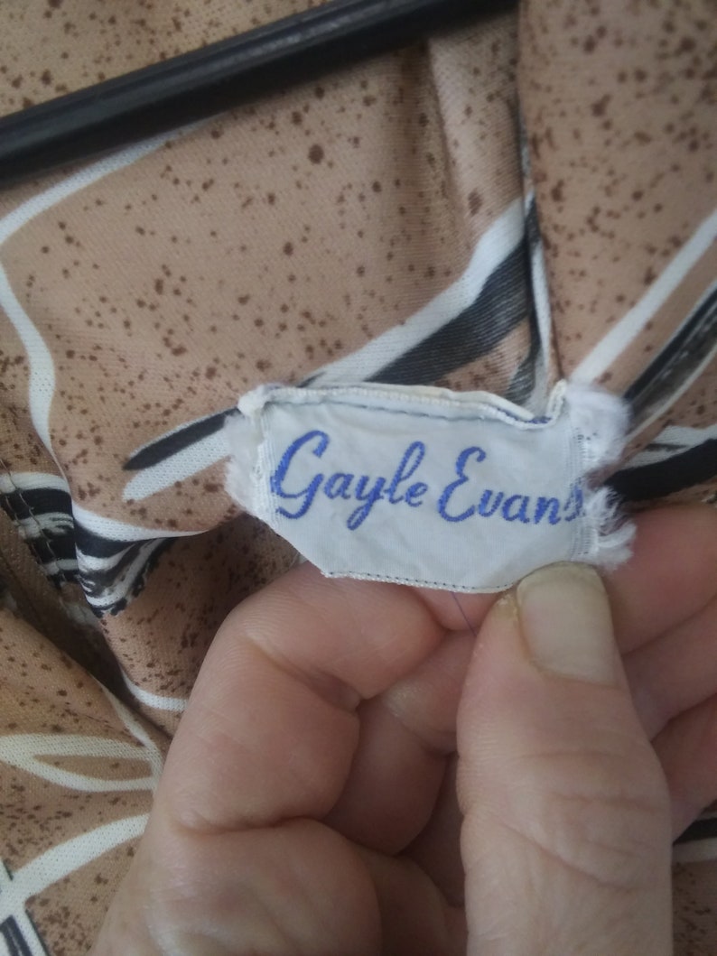 May include: A white tag with blue text that reads "Gayle Evans" on a brown and white striped fabric.