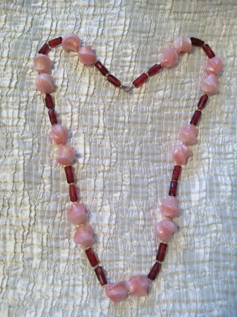 Peut inclure: Un collier de perles rose et bordeaux avec des perles en forme de c&oelig;ur. Le collier est fait de perles de verre et est enfil&eacute; sur une cha&icirc;ne en argent.