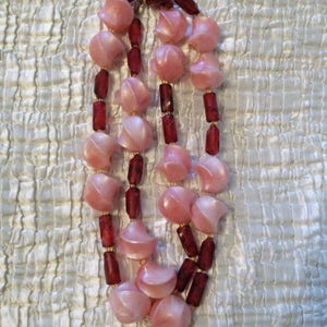 Peut inclure: Un collier &agrave; double rang de perles roses et bordeaux. Les perles roses sont en forme de croissant de lune et les perles bordeaux sont rondes.