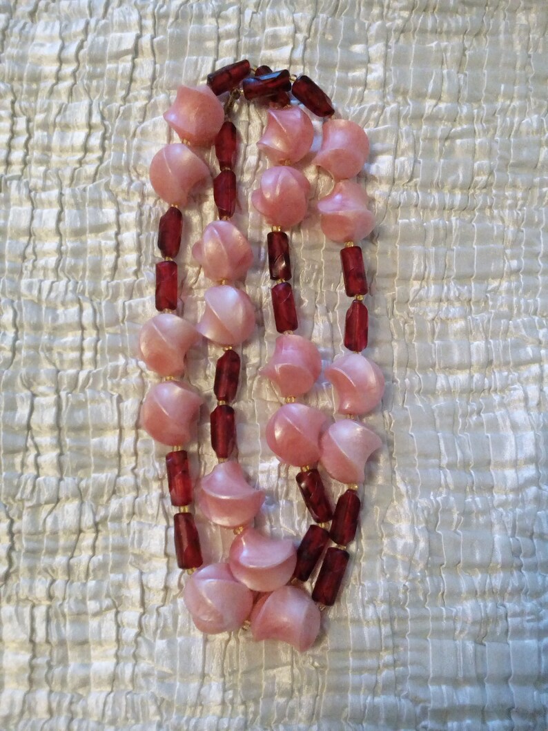 Peut inclure: Un collier &agrave; double rang de perles roses et bordeaux. Les perles roses sont en forme de croissant de lune et les perles bordeaux sont rondes.