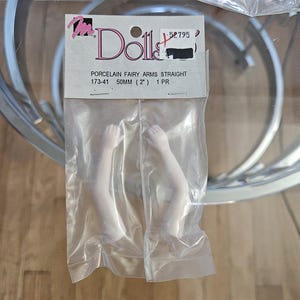 May include: A package of porcelain doll arms, straight, in a clear plastic bag. The label reads "Dolls" and "Porcelain Fairy Arms Straight 173-41 50mm (2") 1 PR". The arms are white and appear to be for a fairy doll.