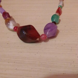 Pu&ograve; includere: Una collana di perline colorate con perline di diverse forme e dimensioni. Le perline sono in vetro e hanno una variet&agrave; di colori, tra cui rosso, verde, viola e bianco.