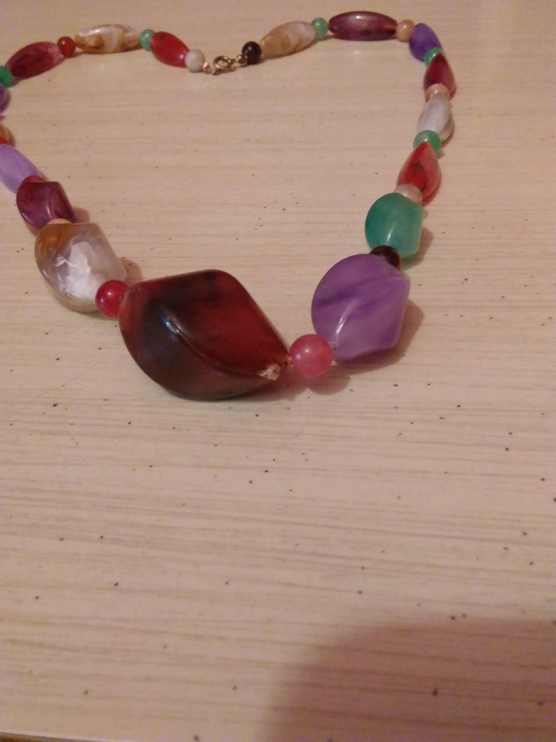 Pu&ograve; includere: Una collana di perline colorate con perline di diverse forme e dimensioni. Le perline sono in vetro e hanno una variet&agrave; di colori, tra cui rosso, verde, viola e bianco.