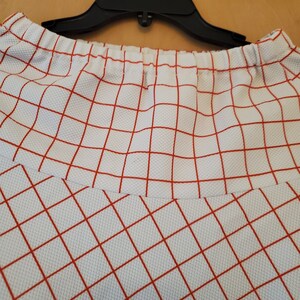 May include: White skirt with a red checkered pattern. The skirt has an elastic waistband.