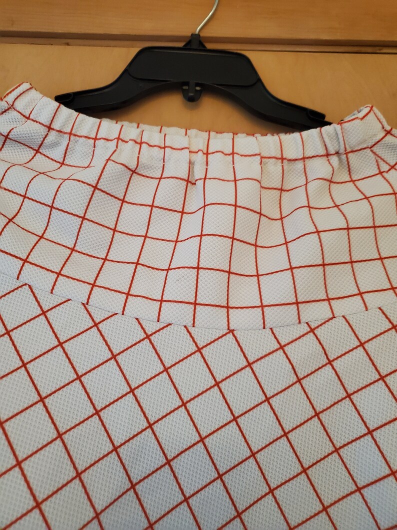 May include: White skirt with a red checkered pattern. The skirt has an elastic waistband.