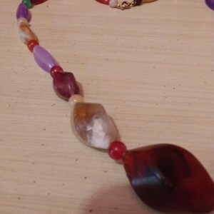 Pu&ograve; includere: Una collana di perline multicolori con una variet&agrave; di forme e dimensioni. Le perline sono fatte di vetro e plastica e sono infilate su un filo trasparente. La collana &egrave; chiusa con una chiusura in metallo.
