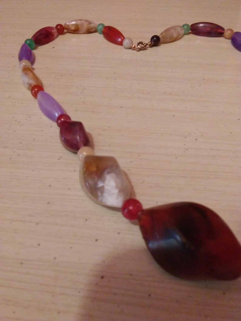Pu&ograve; includere: Una collana di perline multicolori con una variet&agrave; di forme e dimensioni. Le perline sono fatte di vetro e plastica e sono infilate su un filo trasparente. La collana &egrave; chiusa con una chiusura in metallo.