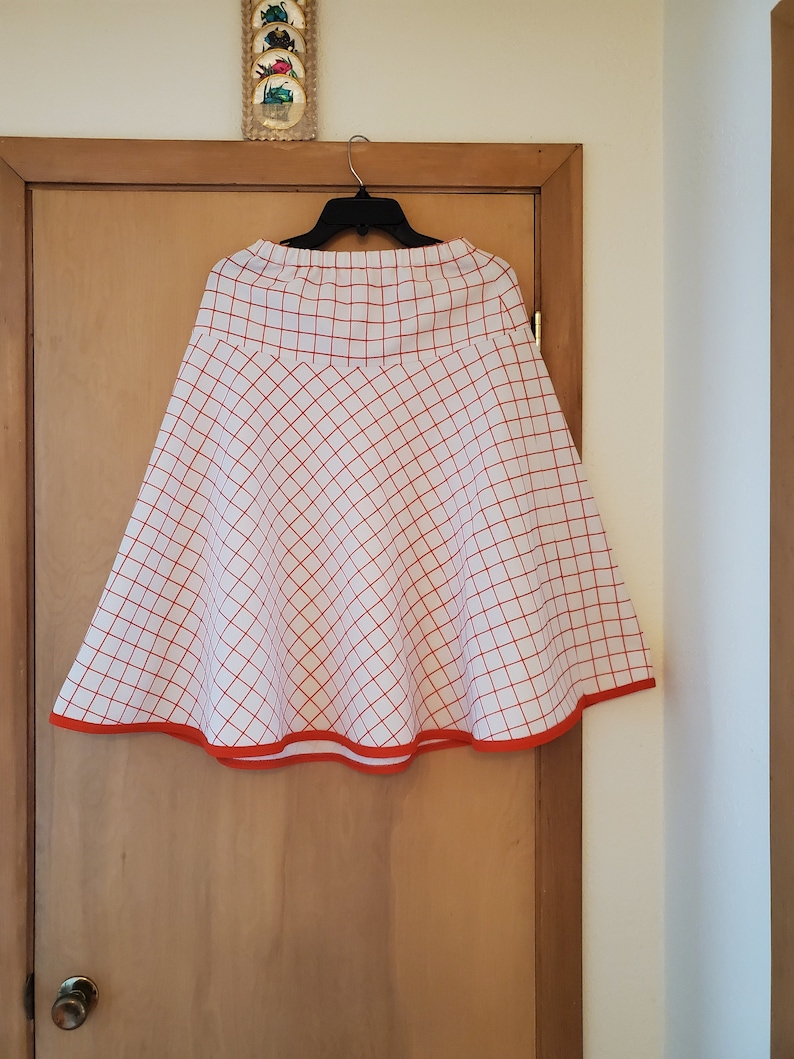 May include: A white skirt with a red and white checkered pattern and a red trim around the bottom.