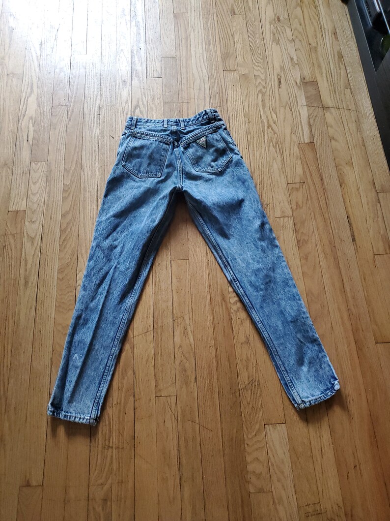 May include: Light blue denim jeans with a faded wash and a triangular logo on the back pocket.