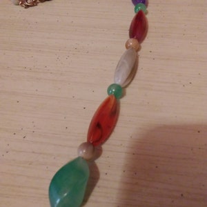 Pu&ograve; includere: Una collana di perline multicolori con perline di forma ovale e a goccia. Le perline sono in vetro e hanno una variet&agrave; di colori, tra cui rosso, verde, viola e bianco.