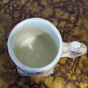 May include: A white ceramic mug with a brown handle and a floral design. The mug is empty and has a white interior.