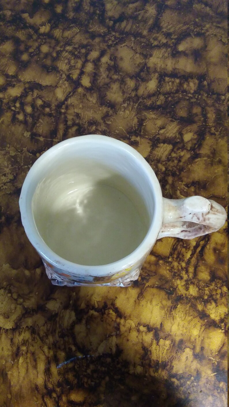 May include: A white ceramic mug with a brown handle and a floral design. The mug is empty and has a white interior.