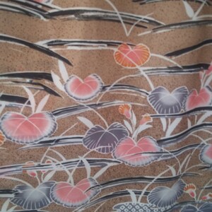 May include: A brown fabric with a repeating pattern of pink, orange, and gray flowers. The flowers are stylized and have a watercolor effect. The background is a light brown with a subtle texture.
