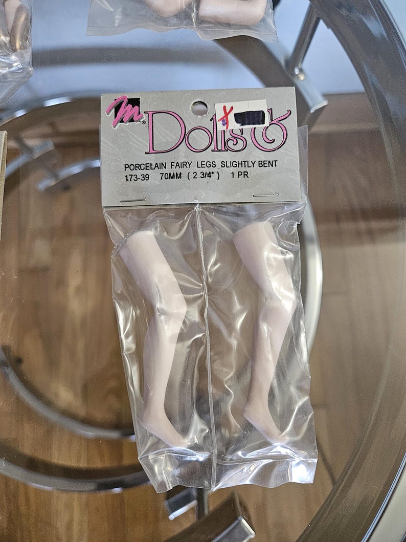 May include: A package of porcelain fairy legs, slightly bent, in a clear plastic bag. The legs are a pale flesh tone and measure 2 3/4 inches (70mm) in length. The package has a label with the words "Mr. Doll's".