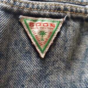 May include: A triangular denim patch with a white background and green border. The text "SOON 100% COTTON LOS ANGELES NEW YORK" is printed in red.