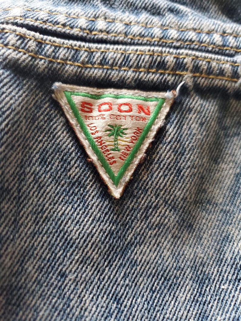 May include: A triangular denim patch with a white background and green border. The text "SOON 100% COTTON LOS ANGELES NEW YORK" is printed in red.