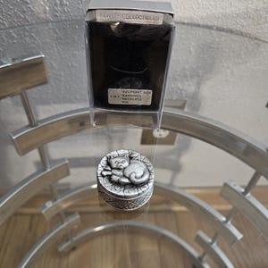 May include: A silver pewter keepsake box with a cat design. The box is labeled "Keepsake Box" and "Earring, Necklace, Pin".