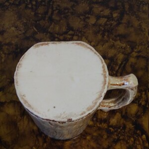 May include: A white ceramic mug with a brown rim and a handle. The mug has a rustic, handmade look.