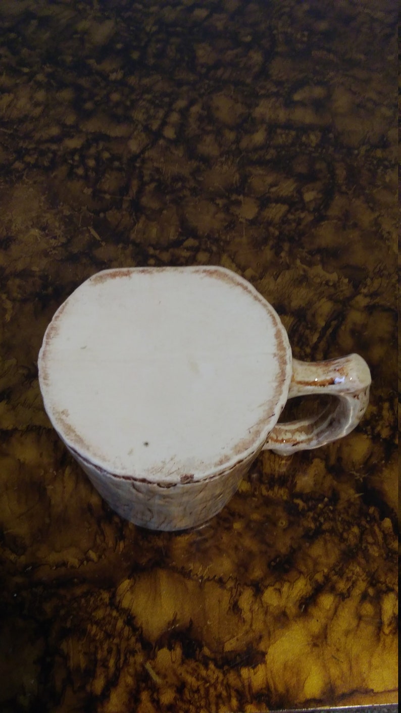 May include: A white ceramic mug with a brown rim and a handle. The mug has a rustic, handmade look.