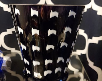 May include: A black glass vase with a white geometric pattern. The vase has a wide mouth and a narrow base.