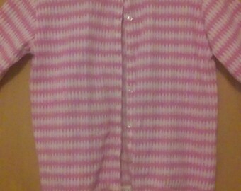 Può includere: Un cardigan a righe rosa e bianche con un bordo in pizzo bianco intorno al collo e all'orlo. Il cardigan ha una chiusura con bottoni.